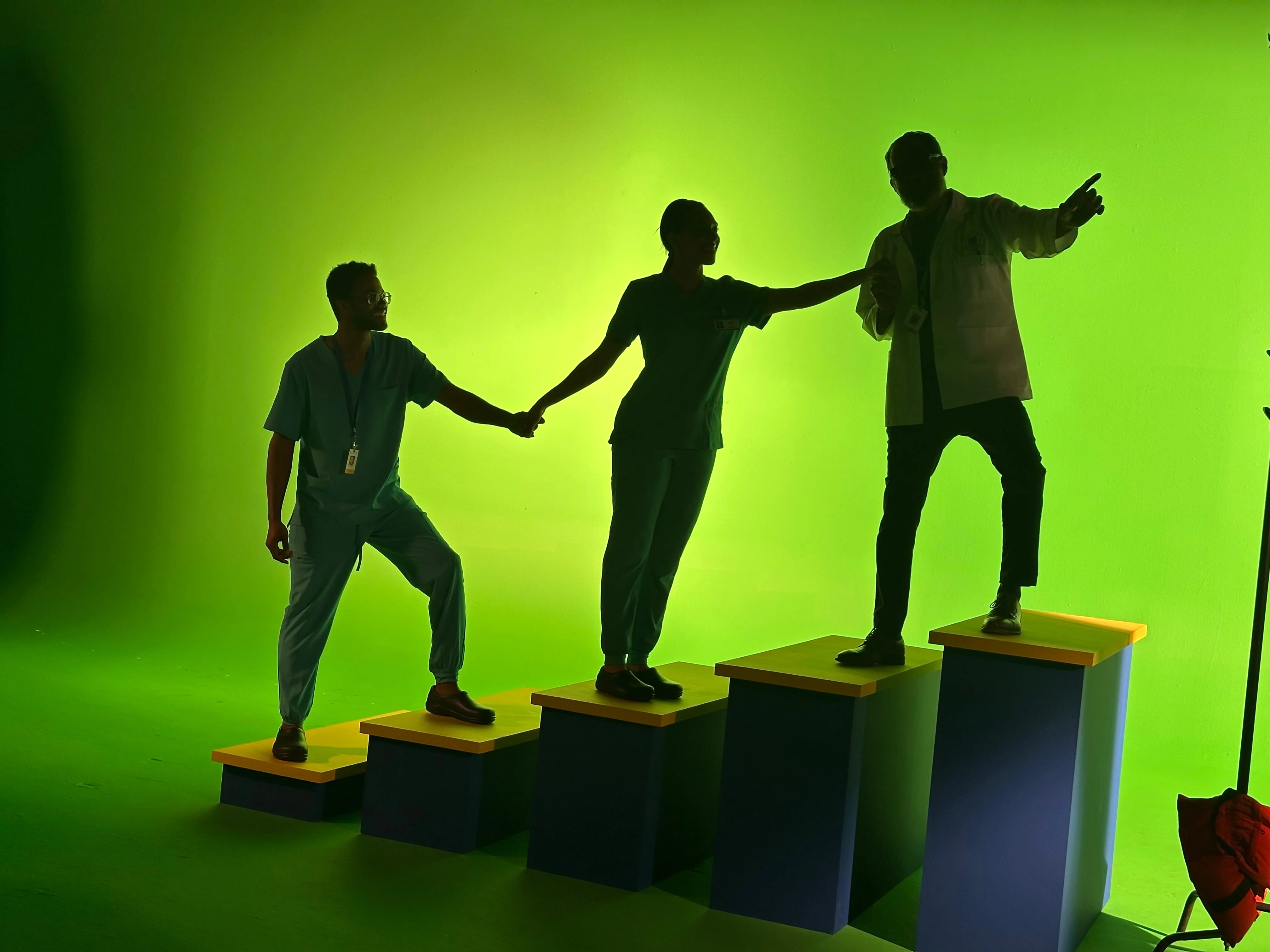 Anthony and two fellow performers linking hands on graduated platforms against a green screen