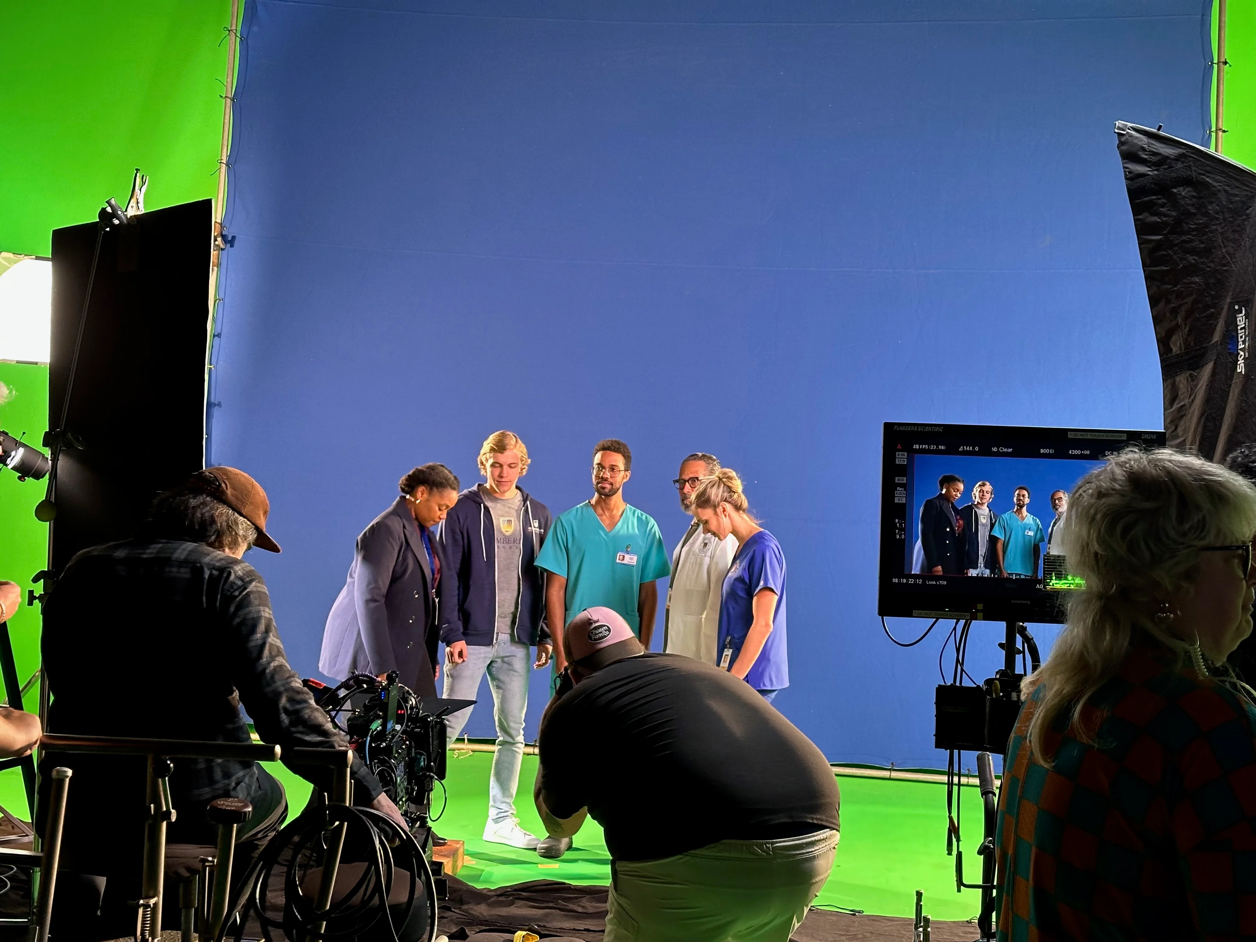 Chamberlain performers on the blue-background set, with the camera crew and production monitor in the foreground