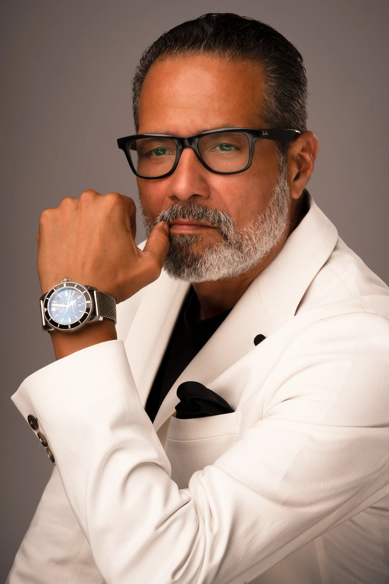 Actor and model Anthony Rolón in a white jacket and black glasses, with his hand and watch beside his face